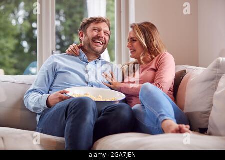 Paar auf Date Night sitzen auf dem Sofa zu Hause lachen und Fernsehen mit Popcorn Stockfoto