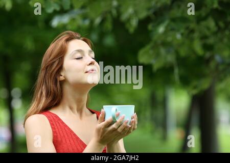 Eine entspannte Frau hält eine Tasse Kaffee und atmet frische Luft in einem Park Stockfoto