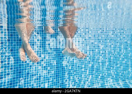 Unterwasser Aufnahme Von Paaren Beine, Wie Sie Sitzen Am Rand Des Schwimmbades Im Urlaub Stockfoto