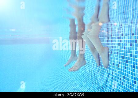 Unterwasser Aufnahme Von Paaren Beine, Wie Sie Sitzen Am Rand Des Schwimmbades Im Urlaub Stockfoto