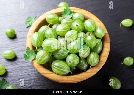 Frische Stachelbeeren in Holzschale auf schwarzem Stein Schiefer Hintergrund. Draufsicht. Stockfoto
