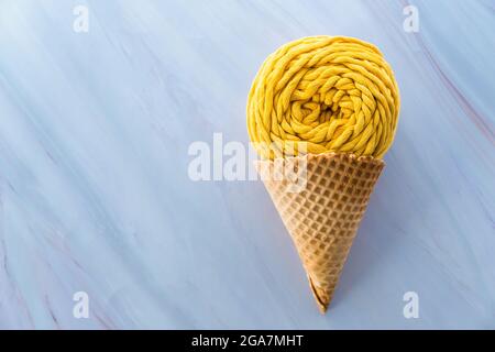 Flache Laie aus gelbem Macrame-Garn-Skein in Eiswaffelkegel auf Marmorboden Stockfoto