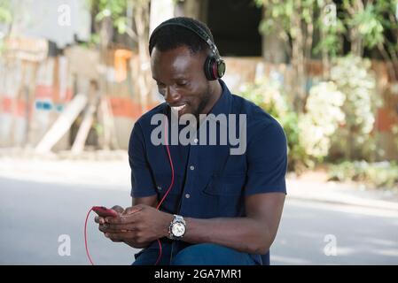 Junger Mann, der mit Kopfhörern im Freien Musik hört, während er auf einem Mobiltelefon zuschaut. Stockfoto