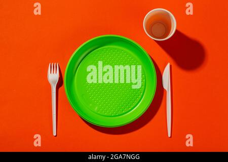 Kunststoff-Set aus Einweggeschirr, bestehend aus Teller, Messer, Tasse und Gabel auf orangefarbenem Hintergrund. Umweltkonzept. Verbot von Einweg-Kunststoff. Stockfoto