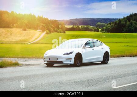 Weißes Tesla Model 3 Elektroauto auf Panoramastraße bei Sonnenschein am Sommermorgen. Salo, Finnland. 24. Juli 2021. Stockfoto