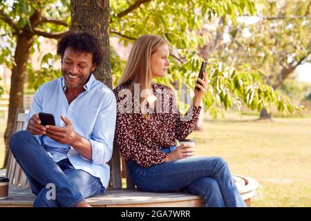 Reifes Paar Treffen Im Outdoor Park Auf Der Bank Sitzend Mit Blick Auf Mobiltelefone Stockfoto