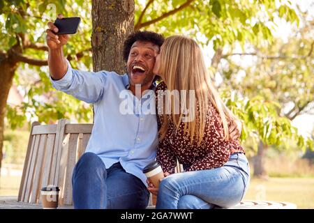 Küssen Älteres Paar Posiert Für Selfie Auf Handy Sitzen Auf Dem Sitz Im Park Stockfoto