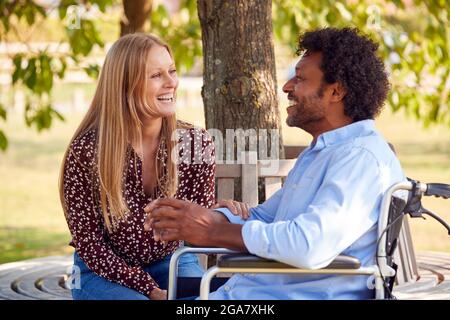 Reifes Paar Mit Mann, Der Im Rollstuhl Sitzt Und Zusammen Im Park Spricht Stockfoto