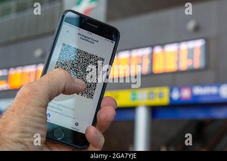 Rom, Italien, Donnerstag, 29. Juli 2021. EU-digitales Covid-Zertifikat Green Pass auf Smartphone vor Zugfahrplänen Stockfoto