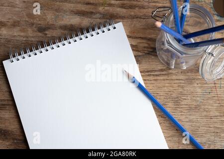 Leeres weißes Papier in einem Notizbuch mit geschärftem Bleistift und einem Glas mit Stiften auf einem alten Holzschreibtisch Stockfoto