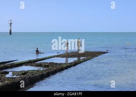 Ein Mann fotografiert die Antony Gormley Statue ein anderes Mal, während ein Fischer im Meer auf Margate Beach, Thanet, Kent, England, Großbritannien schaut Stockfoto