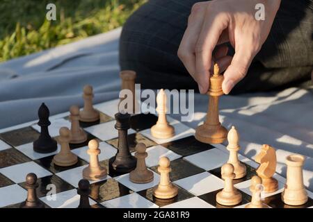 Junger Mann, der eine Bewegung durch Holzschach macht. Schach spielen im Park. Selektiver Fokus. Stockfoto