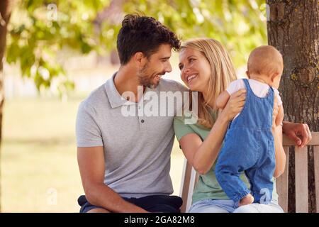 Familie Mit Baby-Tochter Sitzt Auf Seat Under Tree Im Sommer Park Zusammen Stockfoto