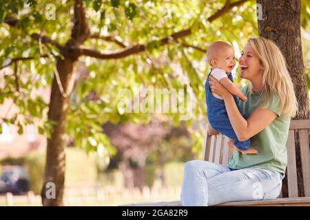 Liebende Mutter Kuscheln Und Spielen Mit Baby-Tochter Im Freien Sitzen Auf Sitz Unter Sommerbaum Stockfoto
