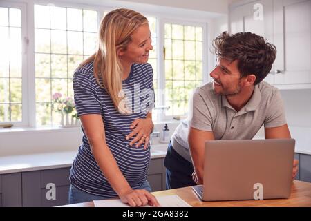 Paar Mit Schwangeren Frau Zu Hause Kauf Von Produkten Oder Dienstleistungen Online Mit Laptop Stockfoto