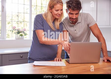 Paar Mit Schwangeren Frau Zu Hause Kauf Von Produkten Oder Dienstleistungen Online Mit Laptop Stockfoto