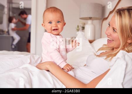 Liebevolle Mutter Im Bett Spiel Mit Baby-Tochter Als Vater Und Sohn Pinsel Zähne Stockfoto