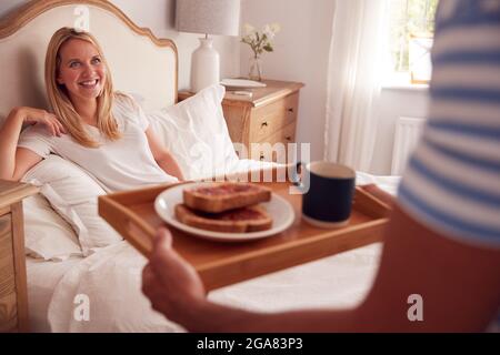 Ehemann Überraschend Frau Mit Frühstück Im Bett Zu Hause Stockfoto