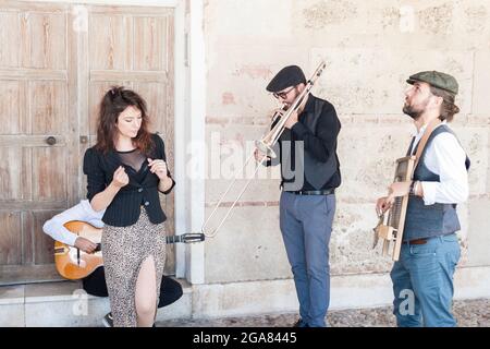 Eine Jazzband, die auf der Straße spielt und singt. Im Vintage-Stil gekleidet. Es gibt einen Sänger, einen Posaunisten, einen Mann, der Waschbrett spielt und einen Gitarristen. Stockfoto