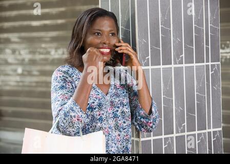 Frau, die draußen gegen eine Wand steht und mit einem Mobiltelefon online einkaufen geht. Porträt einer Frau mit Einkaufstaschen. Stockfoto