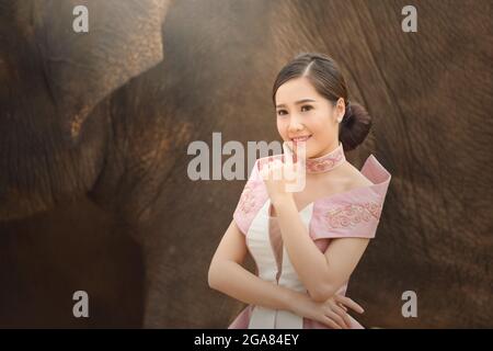 Das Mädchen und der Elefant tragen Blumen.schöne junge asiatische Frau in traditioneller einheimischer Kleidung und Elefant im Wald Des Dorfes Surin Stockfoto