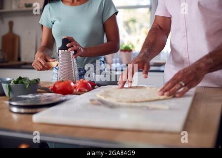 Nahaufnahme Eines Paares In Kitchen At Home, Das Gemeinsam Hausgemachte Pizzas Zubereitet Stockfoto