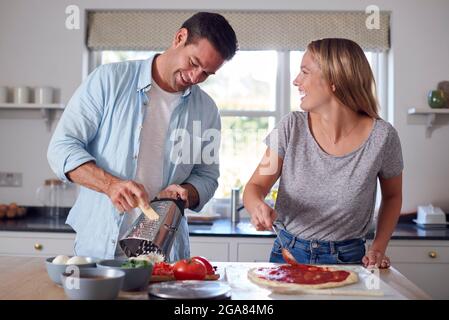 Frau, Die Tomatensauce Auf Der Basis Als Paar In Kitchen Home Verteilen Bereiten Sie Gemeinsam Hausgemachte Pizzas Zu Stockfoto