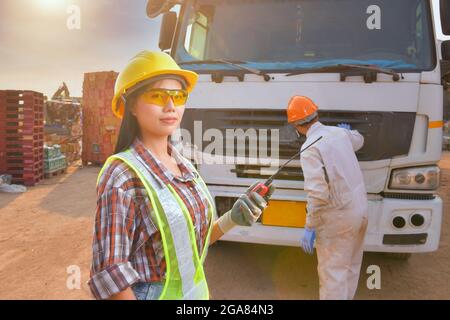 Junge Frau in Schutzkappe mit Waklie-Talkie vor dem LKW-Hintergrund. Stockfoto