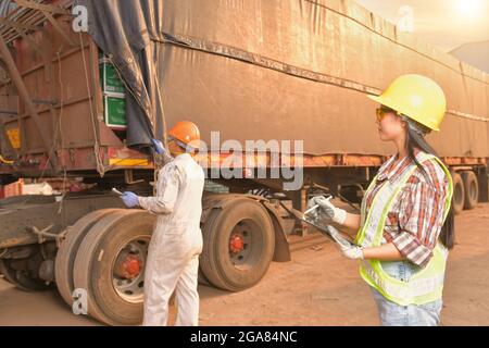 Junge Frau in Schutzkappe hält Tablet vor LKW-Hintergrund. Stockfoto
