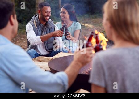 Gruppe Von Freunden Camping Sitzen Bei Bonfire In Fire Bowl Feiern Und Trinken Bier Zusammen Stockfoto