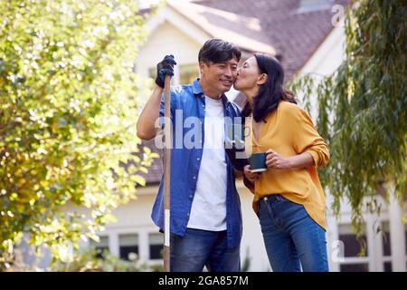 Liebevolle reife asiatische Paar eine Pause mit heißen Getränken während Aufräumen Garten mit Rake Stockfoto