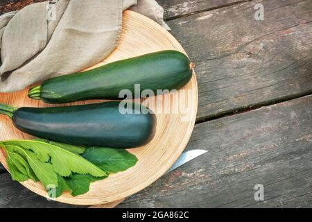 Umweltfreundliche, sommerliche Komposition mit organischen, grünen Zucchini mit Blättern auf einem Teller auf einem Holzhintergrund mit Kopierfläche. Gemüse aus lokalem Anbau Stockfoto