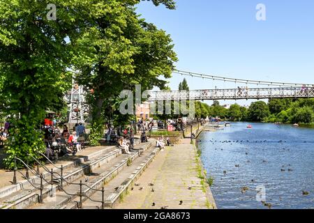 Chester, Cheshire, England - Juli 2021: Menschen, die am Ufer des Flusses Dee sitzen, der durch das Zentrum von Chester fließt Stockfoto