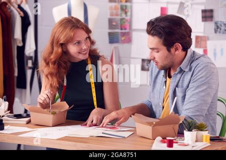 Männliche Und Weibliche Fashion Business Besitzer Diskutieren Designs Über Takeaway Food Im Studio Stockfoto