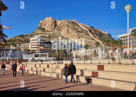 Die Burg von Santa Barbara hoch oben auf einem Vorgebirge mit Blick auf die Stadt Alicante, Spanien, mit der Promenade und den Menschen, die im Vordergrund gehen Stockfoto