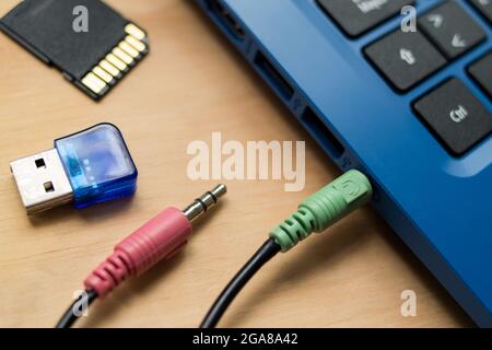 Kopfhörerkabel, die mit einem blauen modernen Laptop verbunden sind, USB-Speicher und SD-Speicher auf einem Holztisch Stockfoto