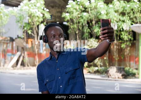 Der Mensch hört mit einem Mobiltelefon Musik mit Kopfhörern und macht Fotos mit seinem Telefon draußen. Stockfoto