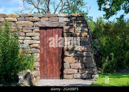 Ein kleines Gebäude aus Schieferstein mit roten Holztüren. Stockfoto