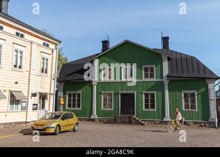 Porvoo, Finnland - 7. Mai 2016: Blick auf die Straße mit bunten finnischen Holzhäusern, Altstadt von Porvoo, Frauen fahren Fahrrad Stockfoto