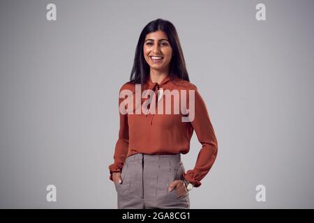 Studio Portrait Of Smiling Young Businesswoman Mit Händen In Den Taschen Vor Dem Hintergrund Stockfoto