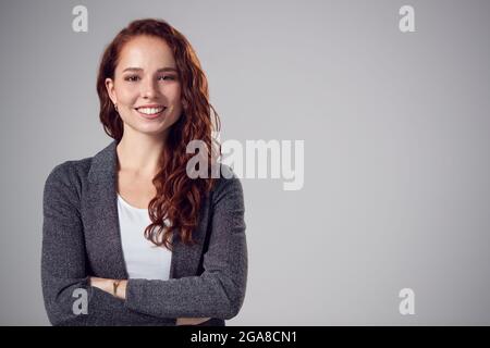Studio Portrait Of Smiling Young Businesswoman With Folded Arms Against Plain Background Stockfoto