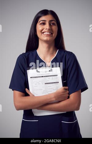 Studio Portrait Der Lächelnden Krankenschwester Mit Zwischenablage, Die Uniform Gegen Einen Einfachen Hintergrund Trägt Stockfoto