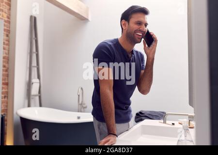 Mann Im Schlafanzug Zu Hause Im Modernen Badezimmer Im Gespräch Mit Dem Mobiltelefon Stockfoto