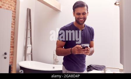 Mann Trägt Schlafanzug Zu Hause Überprüfung Handy In Modernen Badezimmer Stockfoto