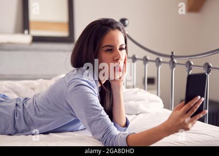 Frau Mit Schlafanzug Am Gesicht, Während Sie Selfie Auf Dem Mobiltelefon Auf Dem Bett Liegend Nimmt Stockfoto