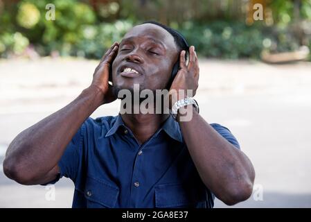 Junger Mann, der im Freien steht und mit Kopfhörern Musik hört, während er lächelt. Stockfoto