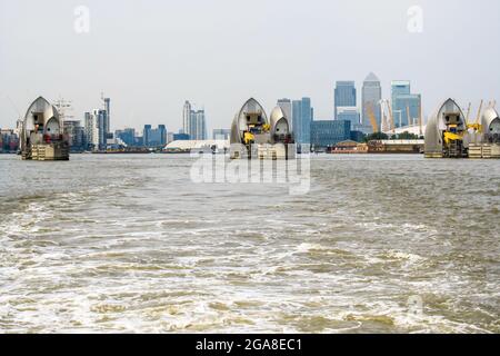 Blick über das Wasser auf die futuristisch anmutende Thames Barrier mit den hohen Anstiegen von Canary Wharf im Hintergrund Stockfoto