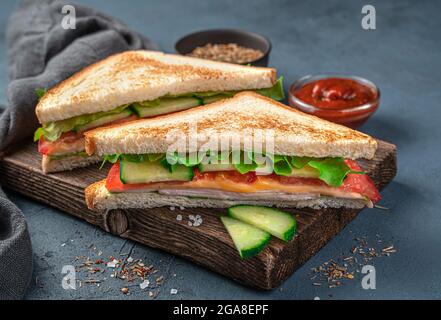 Zwei Sandwiches mit Gemüse, Salat, Schinken und Käse auf blaugrauem Hintergrund. Seitenansicht, Nahaufnahme. Speicherplatz kopieren. Stockfoto