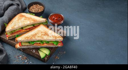 Zwei Schinken- und Käsesandwiches auf einem Holzbrett auf dunkelblauem Hintergrund. Seitenansicht, Kopierbereich Stockfoto