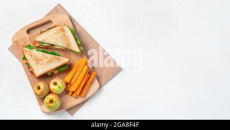 Sandwiches, Äpfel und Karotten auf einem Brett auf einem Kraftbeutel auf grauem Hintergrund. Vorbereitung eines Schulmittags. Draufsicht, Kopierbereich. Stockfoto